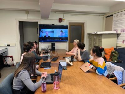 ongoing class at the CHHD with 6 students and Professor Harkness around a table and two students joining virtually visible on a big screen